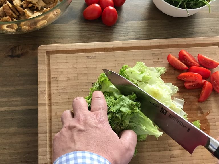 Salat quer in schmale Streifen schneiden, etwas auseinanderzupfen, Tomaten vierteln, alles mit dem Rucola und der Hälfte der Pinienkerne in die Salatschüssel zu den Brotstücken geben. erneut einmal durchmengen.