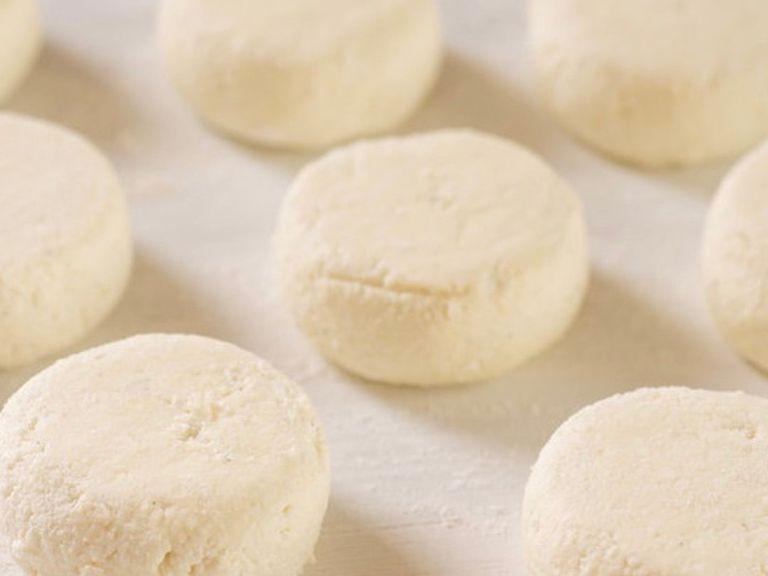 Dust the work surface with flour slightly. Split the cottage cheese mass into equal pieces and roll it into balls. Form the cheesecakes.