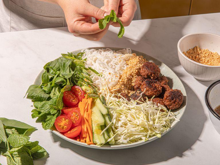 Den Salat auf einzelne Teller oder auf eine große Platte geben. Dabei Thai-Basilikum, Minze, Frühlingszwiebeln, Gurke, Spitzkohl, Möhren und Tomaten am Rand des Tellers arrangieren und Reisnudel-Nester eher mittig platzieren. Fleischbällchen hinzufügen und die Soße in einer kleinen Schüssel zum Salat reichen. Etwas Soße auf den Salat löffeln und bei Bedarf mit geröstetem Sesamöl beträufeln. Mit dem Erdnusspulver bestreuen. Guten Appetit!