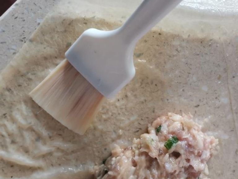 10. Use a brush to apply some egg white on both sides of skin. Fold inwards, similarly apply at bottom of skin and cover the pork mixture, then roll inward slowly, applying some pressure to maintain the roll shape.