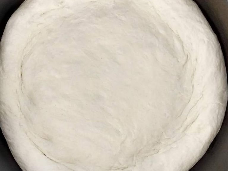 After an hour, put the dough on the table and create pats from it. Start heating the pan and put some olive oil in it. Put the dough pat in the pan and fit the dough to the size of the pan. Put the cover onthe pan and fry the dough on the small heat for 5min.
