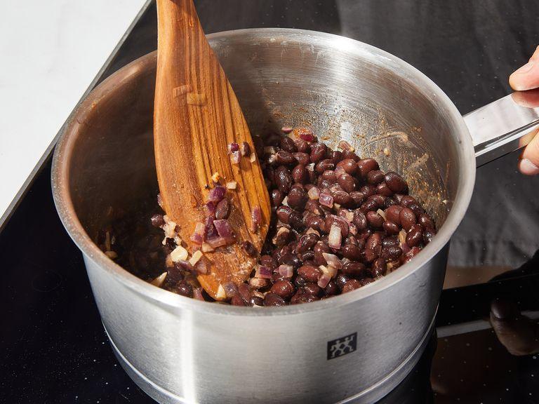 Schwarze Bohnen abgießen und die Flüssigkeit auffangen. Rote Zwiebel und Knoblauch in feine Würfel schneiden. Olivenöl bei mittlerer bis hoher Stufe erhitzen und die Hälfte der Zwiebelwürfel dazugeben. Braten, bis sie glasig werden, dann Knoblauch dazugeben und ebenfalls kurz braten, bis er aromatisch duftet. Bohnen, ein paar Löffel der Bohnenflüssigkeit, Kreuzkümmel, scharfes, geräuchertes Paprikapulver, Salz und Pfeffer in den Topf geben. Köcheln, bis die Bohnen eine cremige Masse ergeben. Dafür ein paar Bohnen mit dem Kochlöffel zerdrücken und, falls nötig, mehr von der Flüssigkeit hinzufügen. Von der Hitze nehmen und zur Seite stellen.