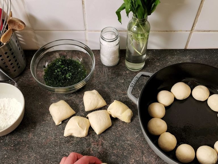 Press the dough down with your fist and divide it into 15 equal pieces, then roll each piece into a ball. Grease an ovenproof skillet with olive oil and place the dough balls in it. Make sure to leave approx. 1 cm/1/3-in. of space between each dough ball. Cover with a damp kitchen towel and let rise for another 30 min.