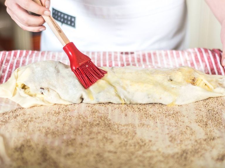 After every fold, brush with melted butter. Repeat this process until the whole strudel is unrolled. Cut the excess dough away from the edges. Make sure the joint is facing down and then use the kitchen towel to place into a suitably sized baking tin .