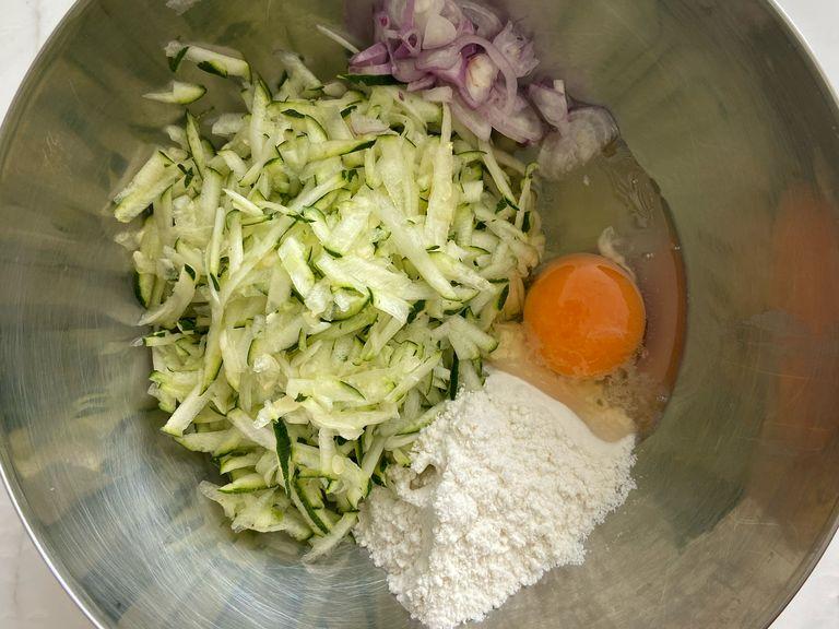 In a large mixing bowl, Add grated zucchini, flour, egg, onions and season with salt and black pepper