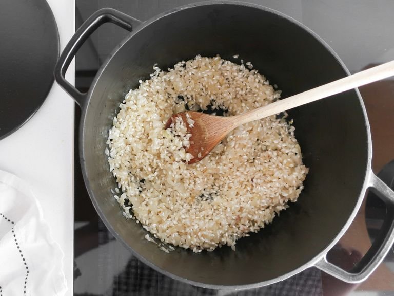 Olivenöl in einer großen Pfanne erhitzen. Zwiebelwürfel bei mittlerer bis hoher Hitze ca. 5-7 Min. anbraten, bis sie glasig sind. Risottoreis dazugeben und gut verrühren. Hitze reduzieren und mit Weißwein ablöschen. Gut umrühren, bis der Weißwein vom Reis aufgesogen wurde. Eine Kelle der Gemüsebrühe zum Reis geben, bis er knapp bedeckt ist. Unter regelmäßigem Rühren die Gemüsebrühe Kelle für Kelle zum Reis geben, aber immer erst damit warten, bis die bisherige Brühe fast vollständig vom Reis aufgesogen wurde. Zum Schluss sollte der Reis al dente sein und die Mischung nicht zu trocken.