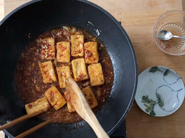 Wenn der Tofu gebraten und die Soße vorbereitet ist, erhitze das Sesamöl in einer Pfanne. Brate die weißen Teile der Frühlingszwiebeln kurz an. Füge den gebratenen Tofu und die vorbereitete Soße hinzu. Stelle sicher, dass der Tofu von beiden Seiten von der Soße umhüllt wird. Decke die Pfanne kurz ab und lasse den Tofu kurz köcheln. Wenn der Großteil der Flüssigkeit eingekocht ist, ist der Tofu fertig! Richte ihn auf einem Teller an und garniere ihn mit Sesam und den grünen Teilen der Frühlingzwiebeln. Guten Appetit!
