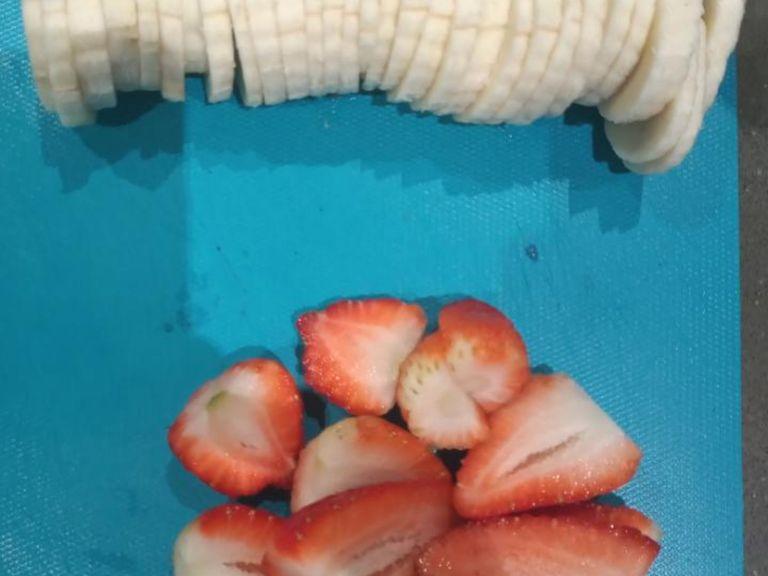 Prepare fresh fruit to serve - cutting banana into slices and strawberries in halves.