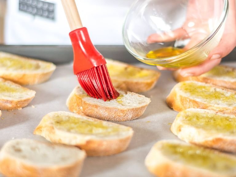 Backofen auf 180°C vorheizen. Baguette in Scheiben schneiden und auf einem mit Backpapier ausgelegten Backblech verteilen. Mit Olivenöl bestreichen und im vorgeheizten Ofen für ca. 10 Min. backen.