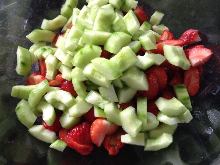 Zuerst wascht ihr die Erdbeeren und viertelt sie. Dann wascht ihr die Gurke, schält sie und halbiert sie. Jetzt kratzt ihr mit einem Teelöffel den weichen, inneren Teil (die Kerne) heraus. Jetzt viertelt ihr beide Hälften und schneidet diese in Stücke. Die Erdbeeren- und Gurkenstücke kommen nun in die große Salatschüssel.