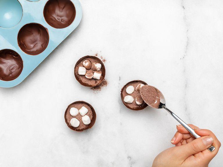 Vorsichtig die Schokoladenhüllen aus der Silikonform entfernen. Mit der Hälfte des gesüßten Kakaopulvers und 1 TL Marshmallow füllen.
