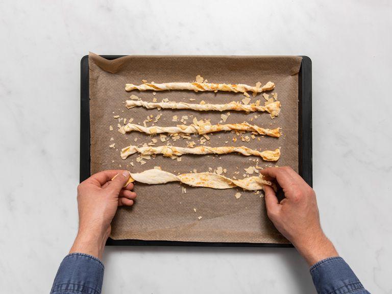 Use a bench scraper or knife to slice the roll into smaller pieces. Transfer to a parchment paper-lined baking sheet, then gently unroll each piece and twist both ends in opposite directions to create a twisted cheese straw. Repeat with all cheese straws.