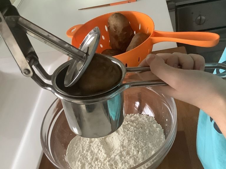 Hover the potatoes over the flour in a potato masher and squeeze all your potatoes in. Remove any excess skin that’s been inserted