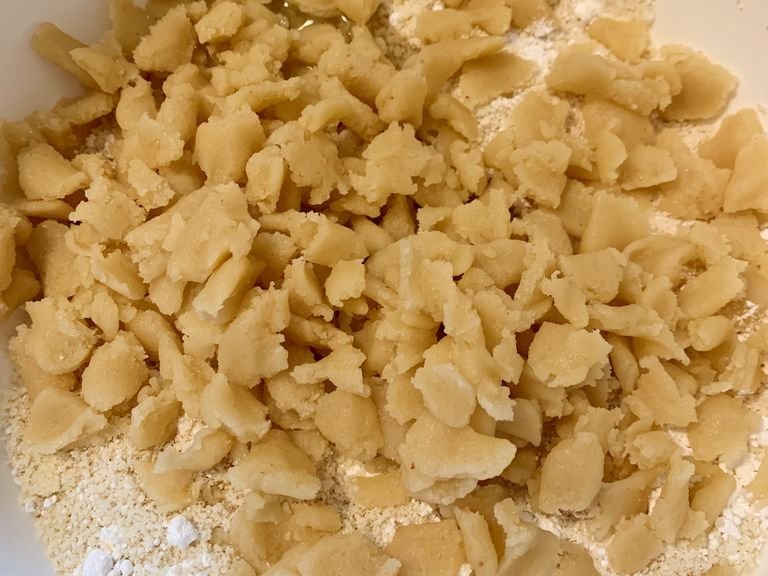 Eiweiß, Amaretto und Zitronenabrieb in die Schüssel geben. Marzipan-Rohmasse in kleine Stücke zupfen und ebenfalls zu den trockenen Zutaten geben. Alles mit den Händen zu einem glatten Teig verarbeiten.
