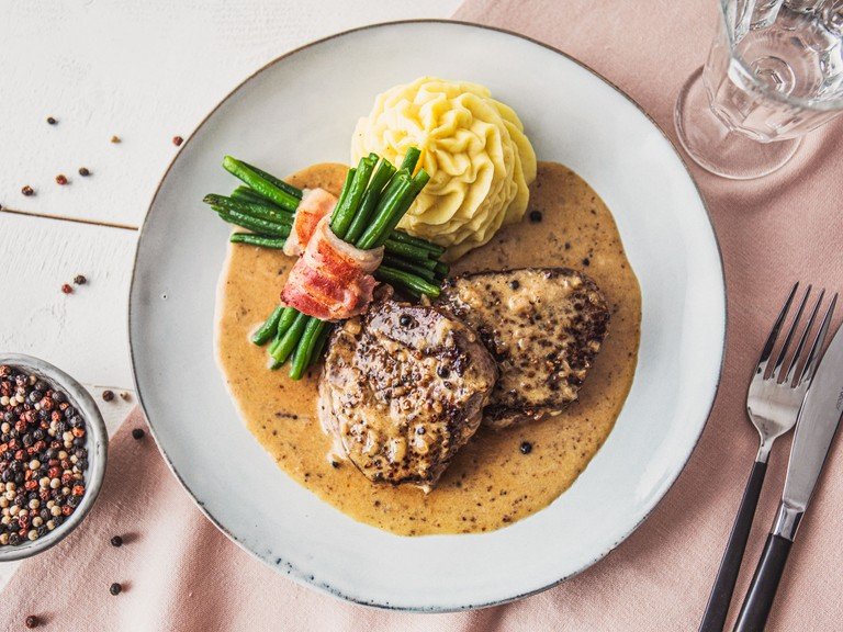 Classic steak au poivre (French pepper steak) with mashed potatoes and green bean bundles