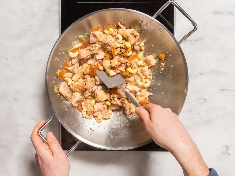 Set a wok over high heat and add half of the sesame oil. Add scallions and dried chili peppers. Then add ginger, garlic, chicken, cashews, and dried apricots. Add remaining sesame oil and season with salt and pepper. Continue frying over medium heat for approx. 4 min.