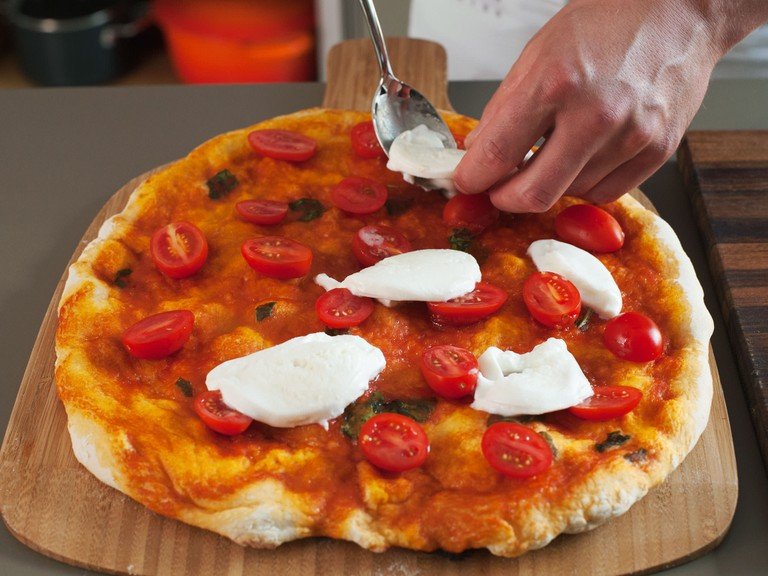 Meanwhile, cut cherry tomatoes in half and buffalo mozzarella into thin slices. Remove pizza from oven; place tomatoes and mozzarella on top, return to oven and bake for another 6 – 7 min. until cheese is melted and crust is golden.