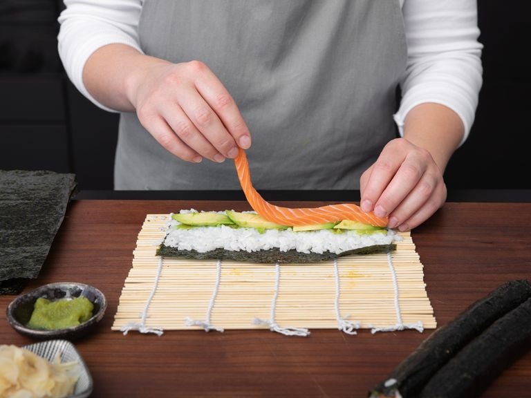 With damp hands, spread cooked sushi rice evenly onto the seaweed sheet. Spread wasabi paste in the center of the sushi rice. Fill with avocado and sweet potato for a vegetarian roll, or salmon and cucumber.