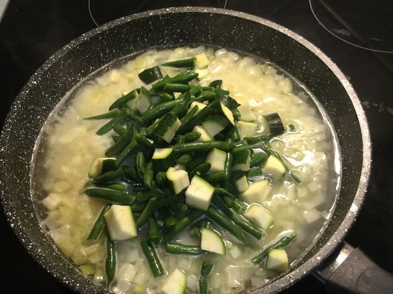 Heat a large frying pan and melt butter. Add the onion and cook until softened before adding the garlic. Add the arborio rice and stir to combine. Then, add two cups off water and leave to boil until first bubbles appear. When mixture starts boiling, add the chopped zucchini and beans.