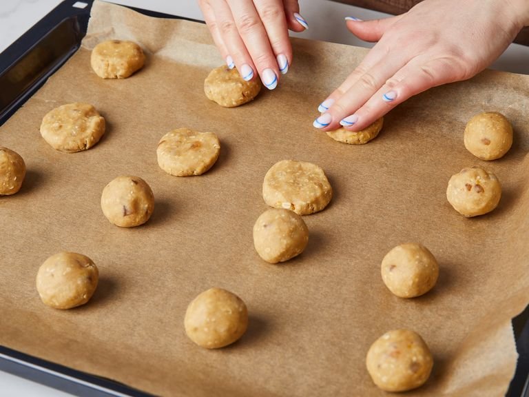 Preheat the oven to 180°C/350°F convection and line two baking trays with parchment paper. After resting, remove cookie dough from the fridge. Roll the dough into little balls, slightly smaller than a ping pong ball (approx. 30 g / 1 oz.). Place cookie balls on the lined baking sheets, making sure there is enough space in-between to allow for spreading. Gently give the balls a light press, but be careful not to make the edges crack too much.