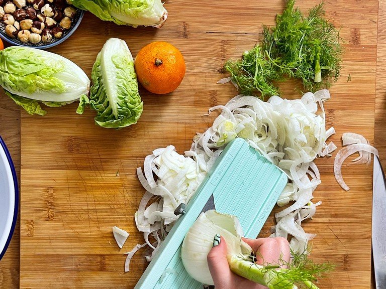 First, cut the fennel into very fine strips with a mandolin. Save the greens to garnish the salad later.