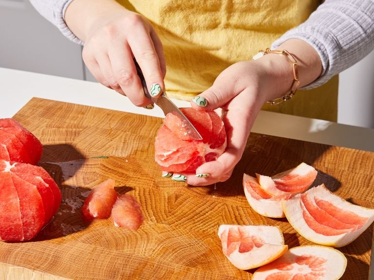 Mit einem großen Messer die Ober- und Unterseite der Grapefruit abschneiden, sodass sie flach auf dem Schneidebrett liegen kann. Dann im Kreis herum die ganze Frucht schälen, indem du die Schale von oben nach unten herunterschneidest. Mit einem Obstmesser die Grapefruit segmentieren und das Fruchtfleisch in eine große Schüssel geben. Die übriggebliebe feste Struktur der Grapefruit auspressen und den Saft in eine kleine Schüssel geben.