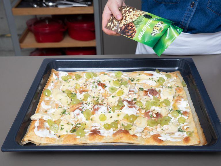 Remove the baked pizza base from the oven and spread cream cheese on it, then top with sliced Brie cheese and halved grapes. Drizzle with honey and sprinkle thyme leaves and pine nuts on top. Season with salt and pepper.