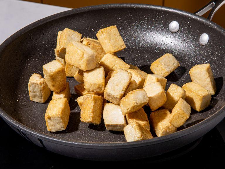 Sesamöl bei mittlerer Stufe in einer Pfanne erhitzen. Den Tofu hinzugeben und ohne zu rühren braten, bis die Unterseite goldbraun ist. Dann umdrehen und weiterbraten, bis alle Seiten goldbraun sind. Aus der Pfanne nehmen und auf einen mit Küchenpapier ausgelegten Teller geben. In einer Schüssel helle Sojasauce, Tomatenmark, Zucker, Reisessig und Gemüsebrühe verquirlen.