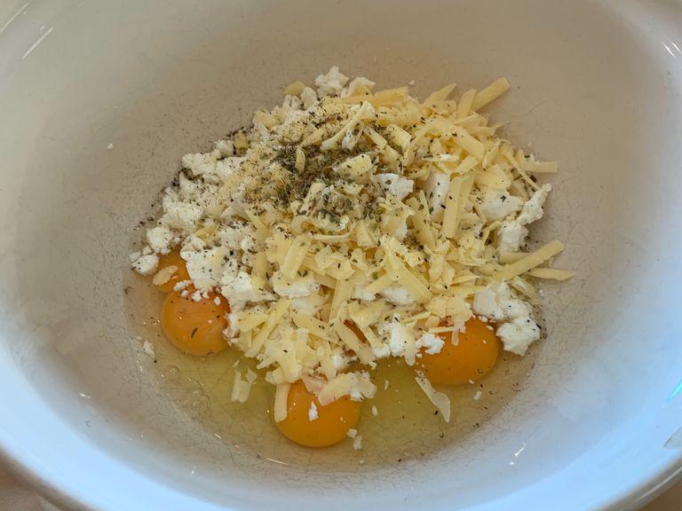 Crack the eggs into a large mixing bowl and crumble the feta . Grate the cheddar, then add the oregano and pepper