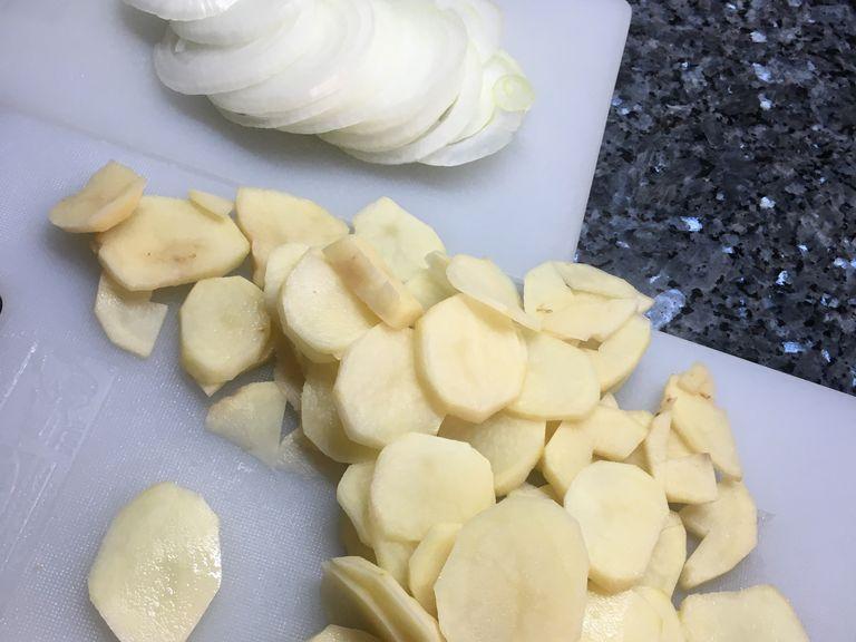 Zwiebel und die geschälten Kartoffeln in Scheiben schneiden.