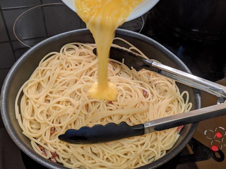 Remove the garlic from the pan. Turn off the heat and drag the spaghetti and a few spoons of the boiling water into the pan. The frying should stop so that you don't hear any sizzling anymore. Now you can add the egg and cheese from the bowl to the pan and stir everything!