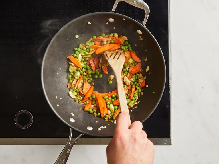 In a wok, heat oil on high heat. Add garlic, onion, carrot, peas, chili, and the white part of the scallion. Sauté for approx. 2–3 min.