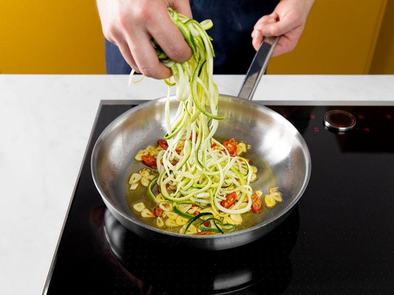 While the pasta cooks, heat half of the olive oil in a large frying pan over medium heat. Add garlic and chili and sauté. Add zucchini and keep frying for approx. 1 min., or until the zucchini is soft.