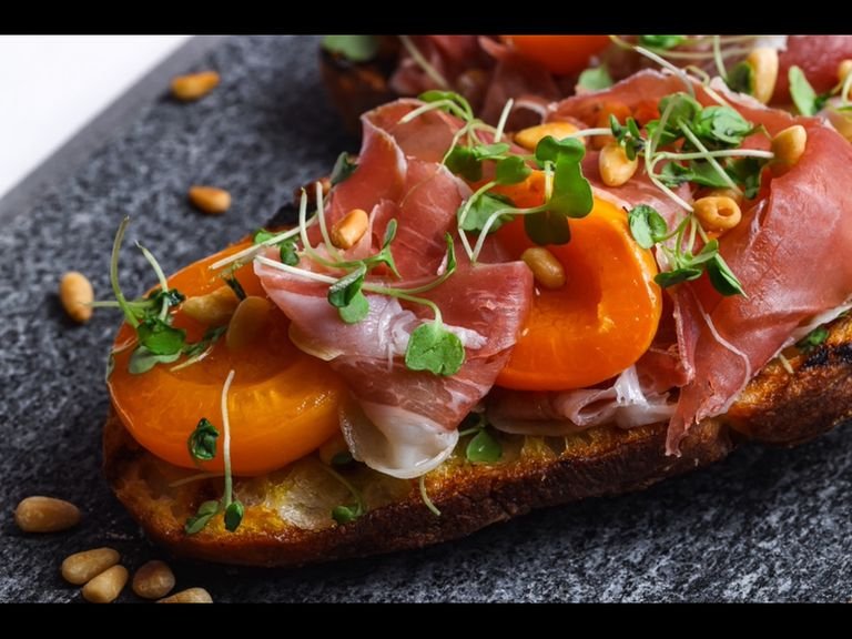 Layer prosciutto and cooked apricots onto grilled bread. Sprinkle on toasted pine nuts and micro arugula. Finish with a drizzle of olive oil.