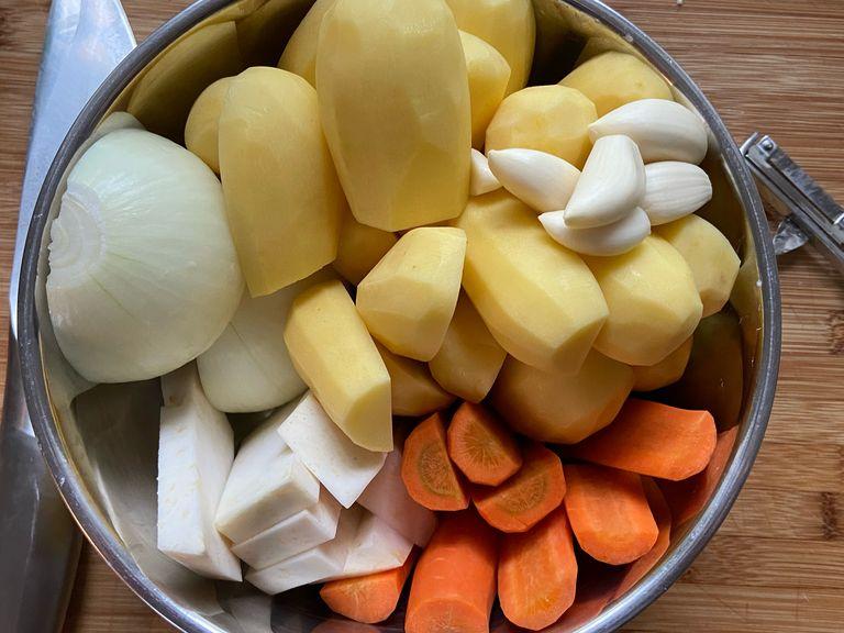 Eine Zwiebel und die Kartoffeln halbieren, die Karotten in halbe Hälften schneiden und den Sellerie in ähnlich große Stücke schneiden.