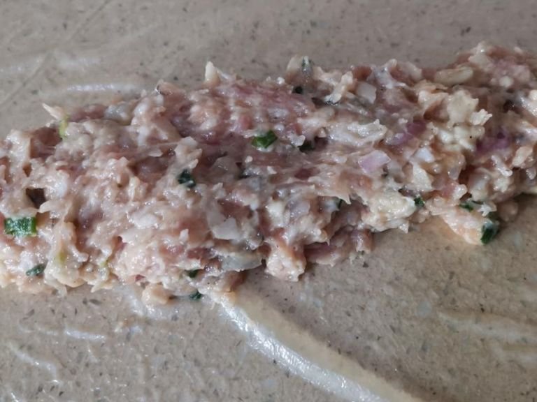 9. Lay out the prepared piece of skin on the work surface. Arrange a heaping tablespoon of the prepared pork mix along the longer edge of the skin, leaving a ½-inch gap from the surrounding edges.