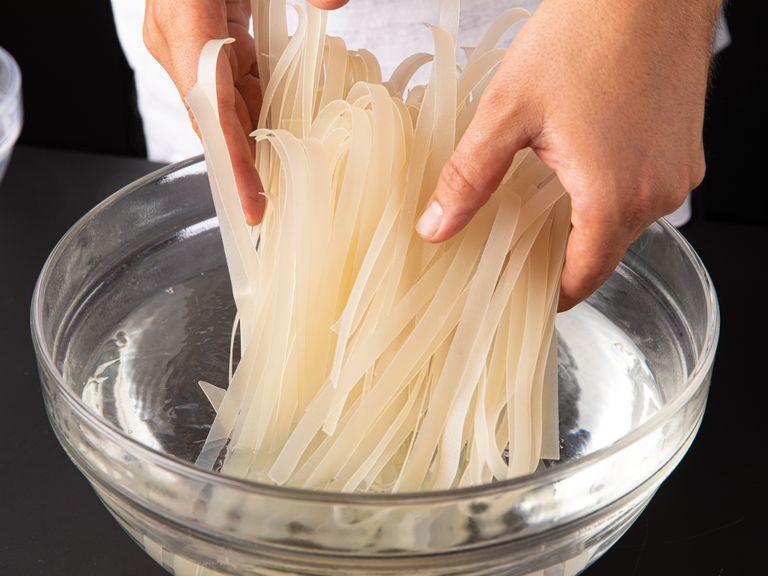 Soak the dried rice noodles in warm water for approx. 15 min. or until soft. Rinse under cold water and drain, and toss them with a little bit of oil to prevent sticking. Slice scallions lengthwise and then cut them into strips, approx. 5 cm/2 in. wide. Slice red onion.