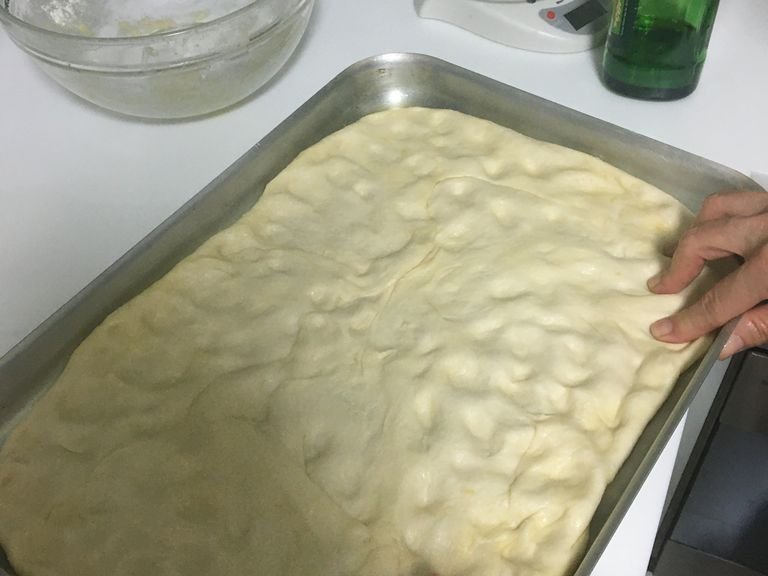 Place the dough out in the pan and spread it until it fills all the corners, using your fingers to create small indentations in the dough. The larger the tray, the thinner the focaccia will become 