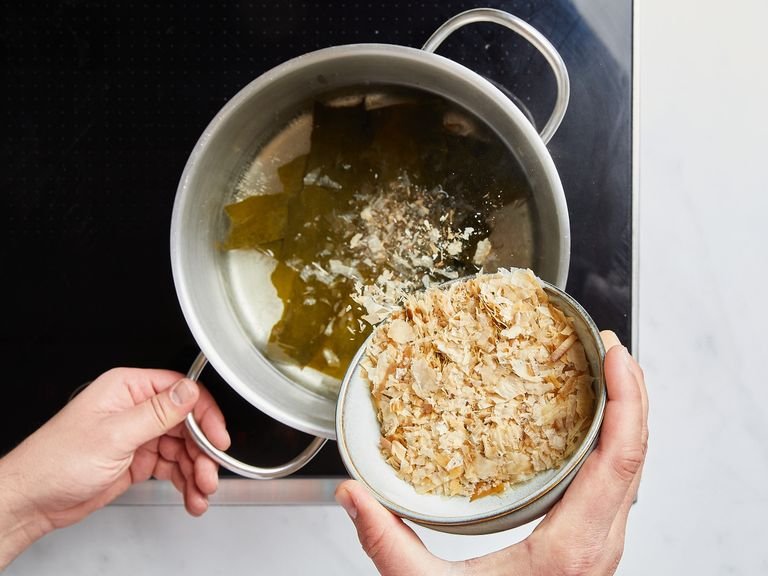 Für die Zubereitung der Dashi (die Brühe für die Suppe) Kombu in einen Topf mit kaltem Wasser geben und auf mittlerer Stufe erhitzen, bis sie leicht köchelt. Ca. 8 – 10 Min. leicht köcheln lassen, bitte nicht kochen lassen! Während des Köchelns den Schaum von der Oberfläche der Dashi abschöpfen. Kombu entfernen, aufkochen lassen und Bonitoflocken hinzufügen. Ca. 1 Min. lang weiterköcheln, dann den Herd ausschalten und ca. 10 Min. lang unbedeckt ziehen lassen. Durch ein feines Sieb über einer Schüssel abgießen, um die klare Dashi aufzufangen.