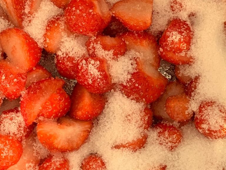 Die Erdbeeren waschen und halbieren. Zucker hinzufügen.