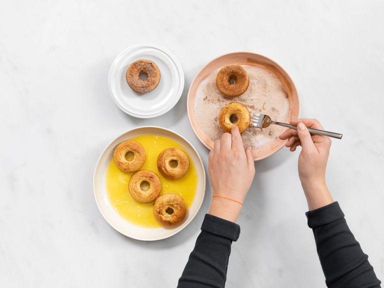 Place the melted butter in a wide, but shallow, dish, then mix the remaining sugar and ground cinnamon in another wide, shallow dish. Gently dip each  donut on both sides into the butter, then into the cinnamon sugar to coat. Transfer back to the cooling rack and serve. Enjoy!