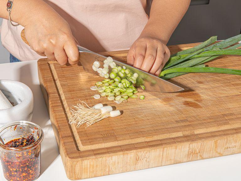 Let frozen wonton wrappers sit at room temperature for approx. 1 hr. Finely mince ginger, thinly slice scallions, and reserve ⅓ of the scallions for serving. To make the garlic water for serving, use a garlic press to press garlic cloves into a small bowl, then add some water and salt.